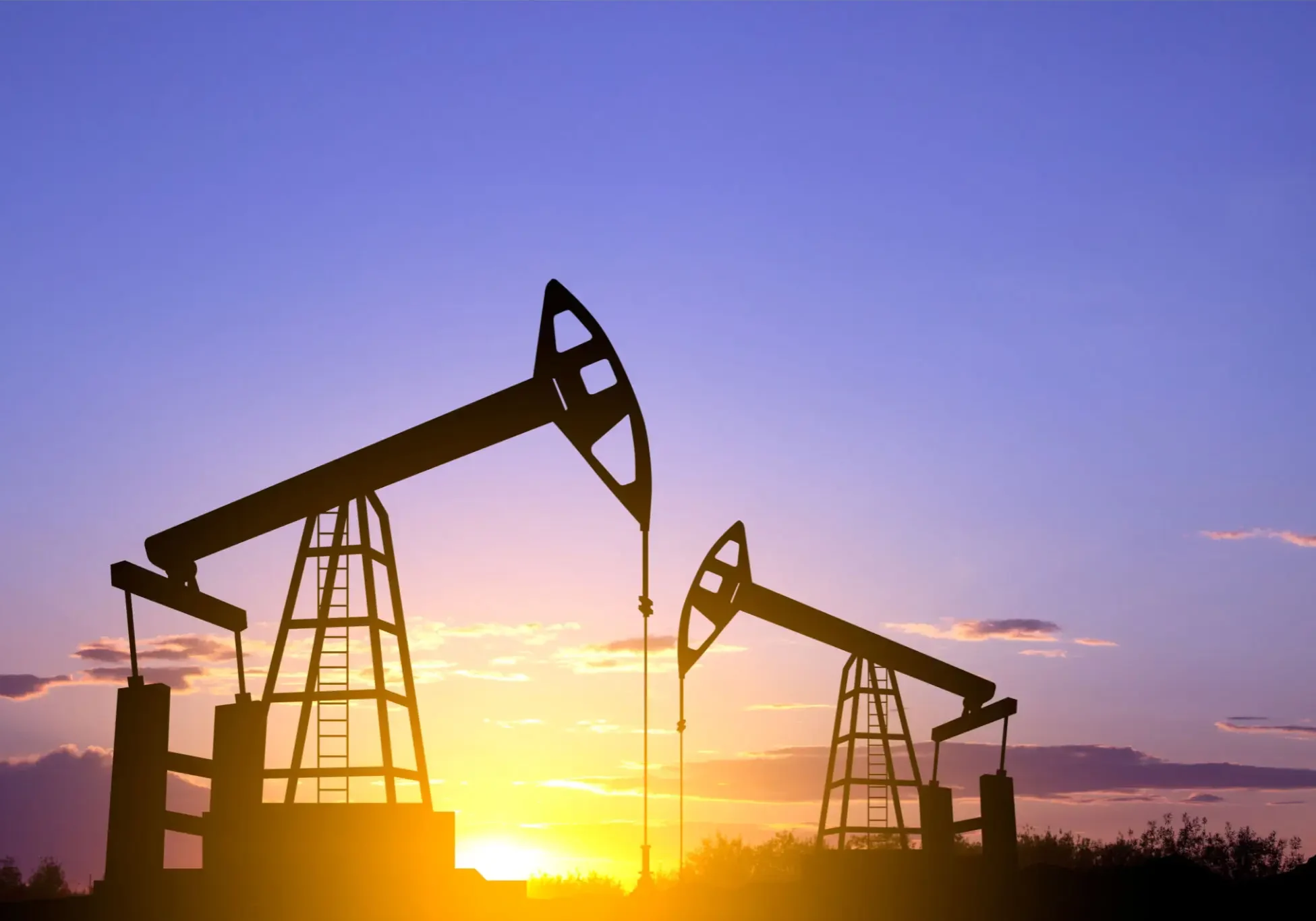 Oil pump jacks silhouetted against a sunset sky.