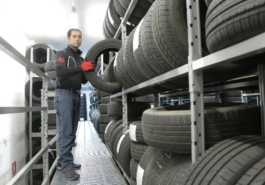 Man standing next to shelves full of tires in a storage room.